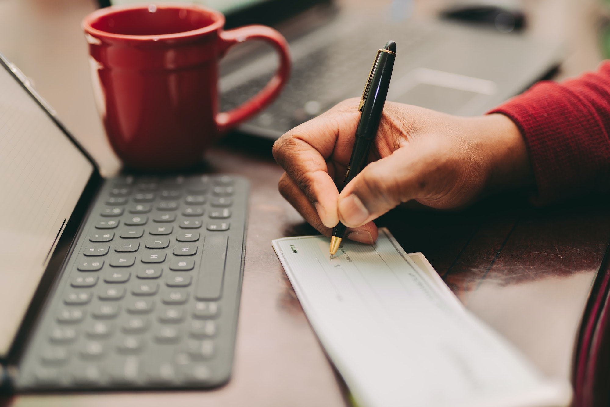 African American man sitting at home office desk writing out a check with a pen